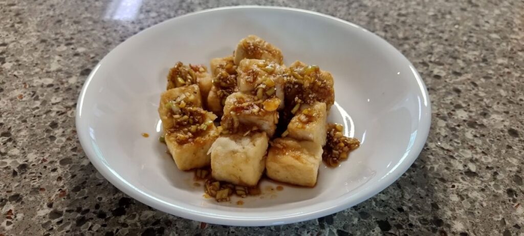 Crispy pan-fried tofu cubes topped with soy scallion sauce on a white plate
